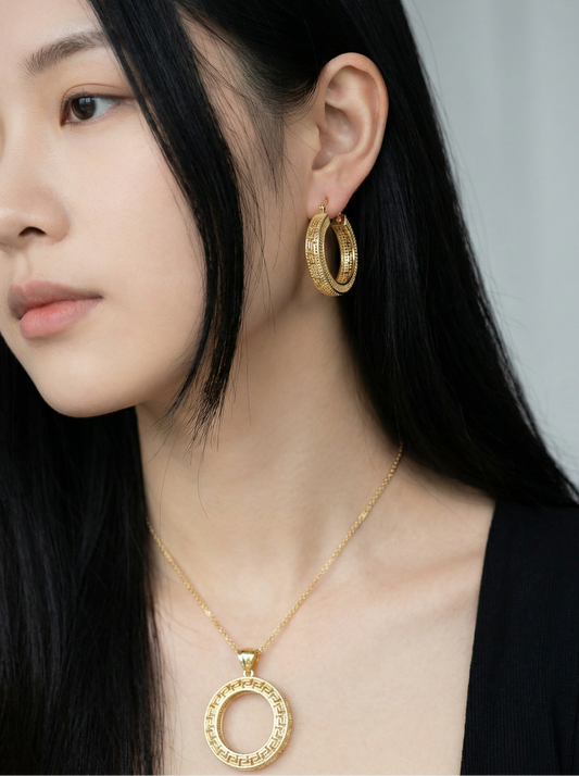 Close-up of a person wearing gold hoop earrings and a gold necklace with a circular pendant.