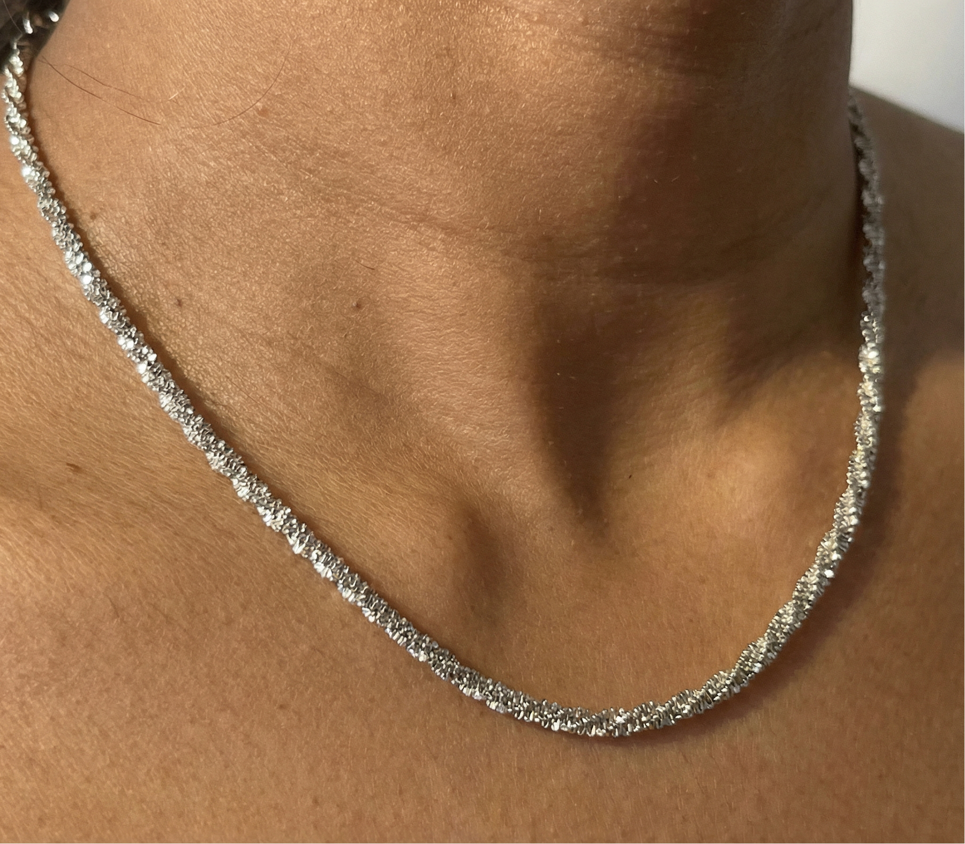 Silver necklace on a person's neck with a neutral background