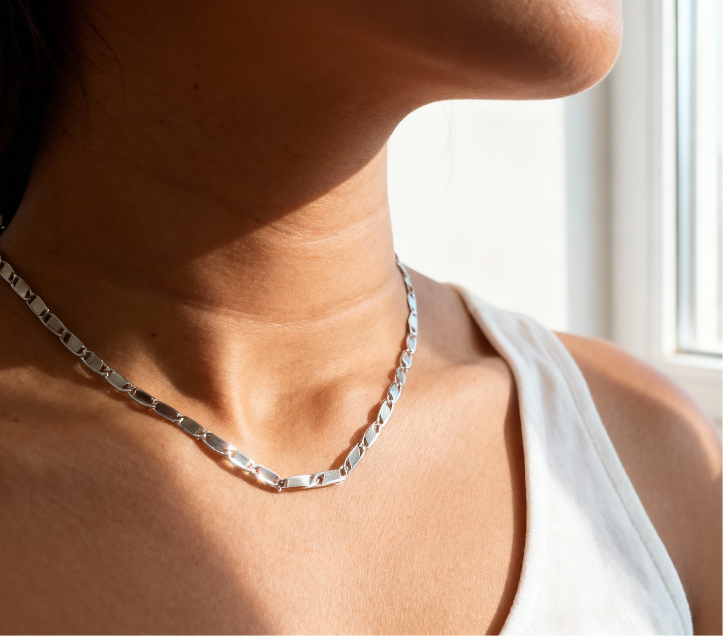 Silver necklace worn by a person with a blurred background