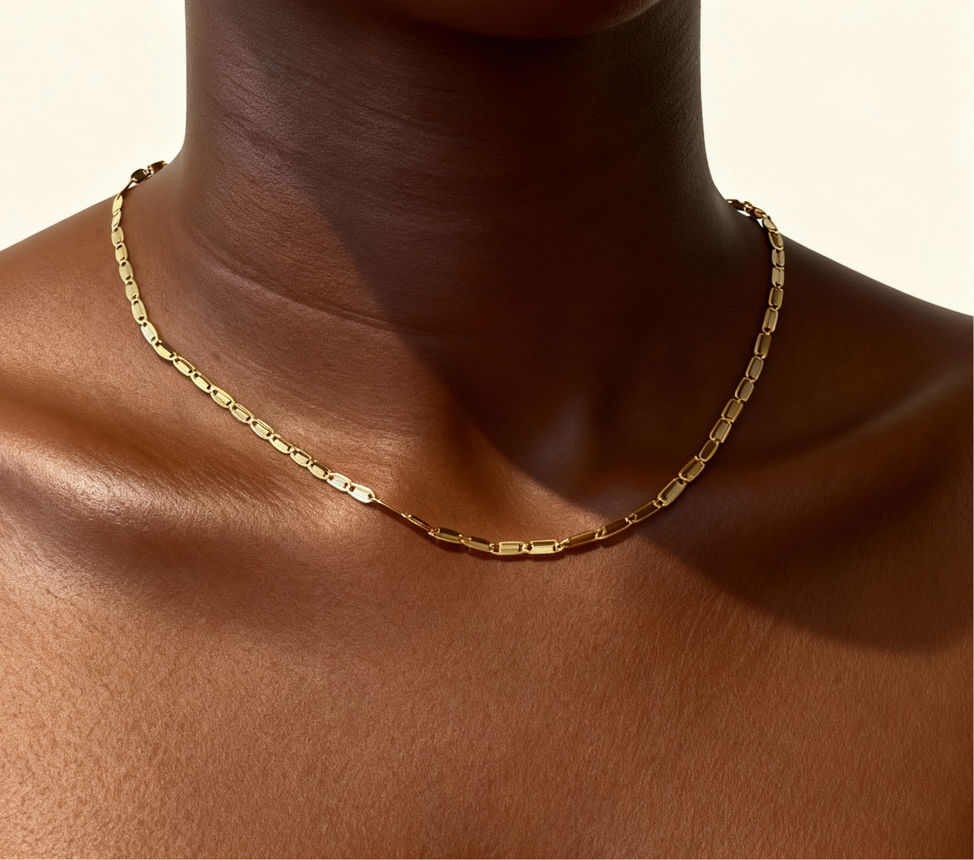 Gold necklace on a person's neck with a neutral background