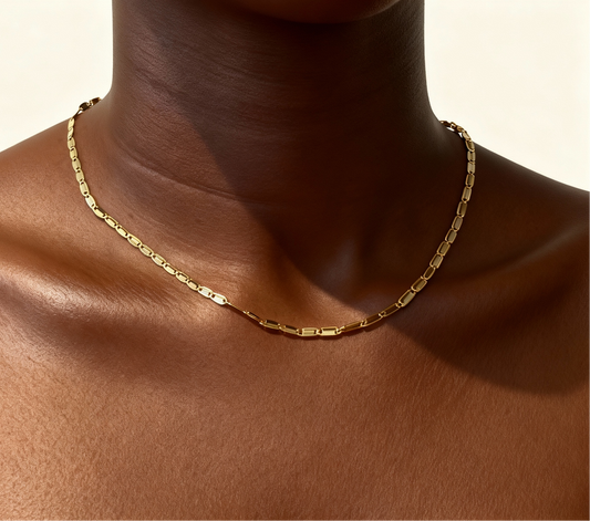 Gold necklace on a person's neck with a neutral background