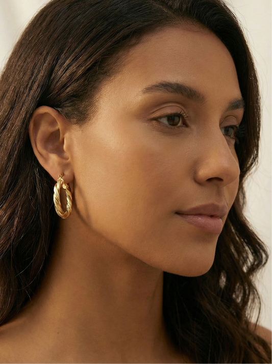Close-up of a woman wearing gold hoop earrings with a neutral background