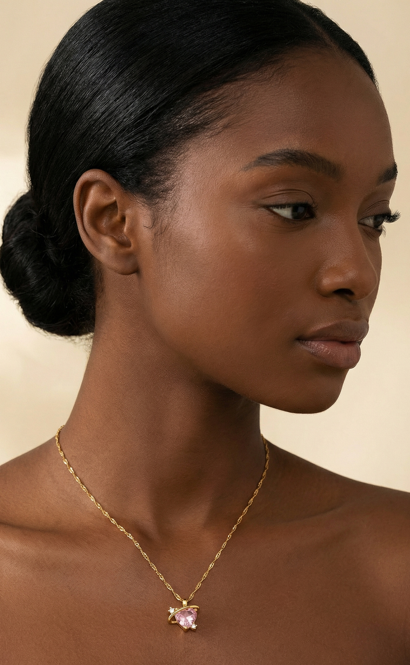 Woman wearing a gold necklace with a pink pendant against a beige background